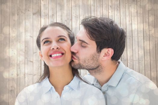 Handsome man kissing girlfriend on cheek against light glowing dots design pattern