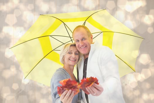 Happy mature couple showing autumn leaves under umbrella against light glowing dots design pattern