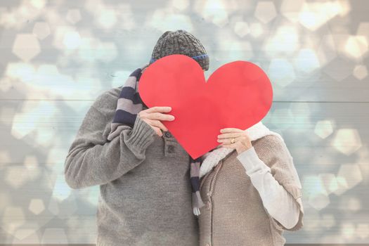 Happy mature couple in winter clothes holding red heart against light glowing dots design pattern