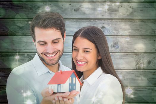 Attractive young couple holding a model house against light design shimmering on green