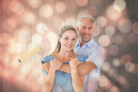 Happy couple hugging and holding paint roller against light circles on black background