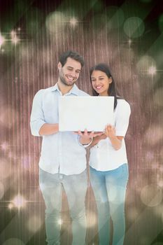 Attractive young couple holding their laptop against light design shimmering on green