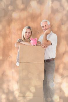 Happy couple leaning on pile of moving boxes with piggy bank against light glowing dots design pattern