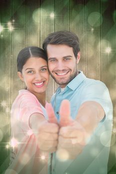 Happy couple showing thumbs up against light design shimmering on green