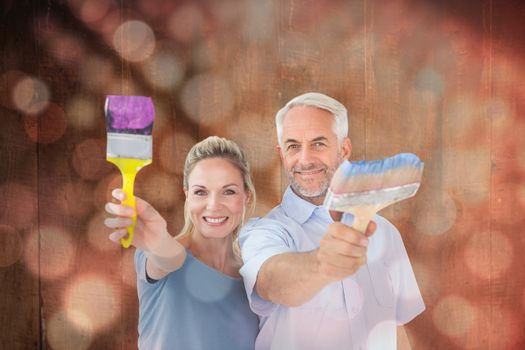 Happy couple holding paintbrushes smiling at camera against light circles on black background