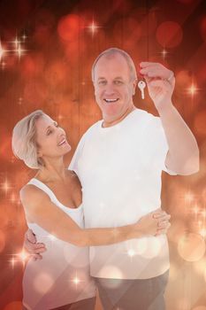 Mature couple smiling at camera with new house key against light design shimmering on red