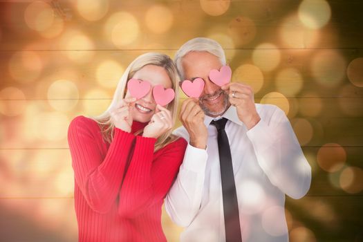 Silly couple holding hearts over their eyes against light circles on black background
