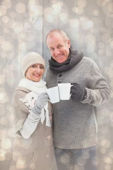 Happy mature couple in winter clothes holding mugs against light glowing dots design pattern