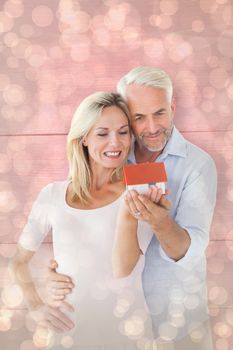 Happy couple holding miniature model house against light glowing dots design pattern