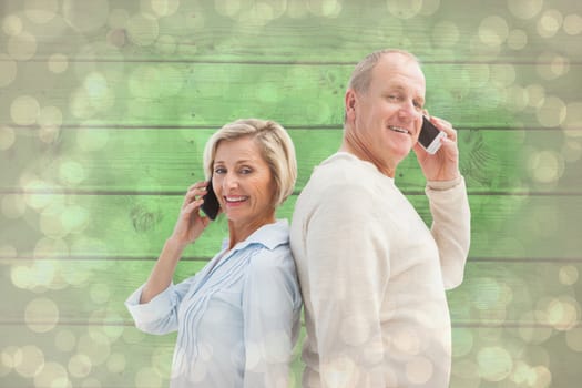 Happy mature couple talking on their phones against light glowing dots design pattern