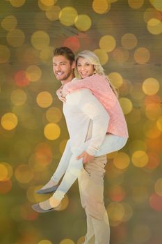 Handsome man giving piggy back to his girlfriend against close up of christmas lights