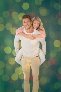 Handsome man giving piggy back to his girlfriend against close up of christmas lights