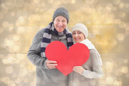 Happy mature couple in winter clothes holding red heart against light glowing dots design pattern