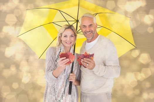 Smiling couple showing autumn leaves under umbrella against light glowing dots design pattern