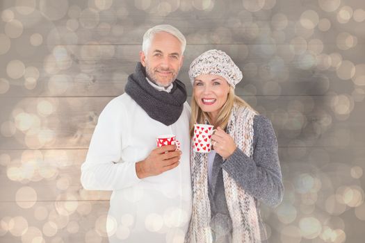 Happy couple in winter fashion holding mugs against light glowing dots design pattern