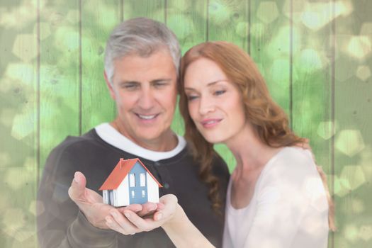 Casual couple holding small house against light glowing dots design pattern
