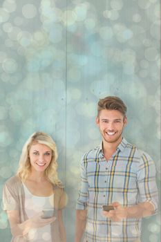 Attractive couple using their smartphones against light glowing dots design pattern