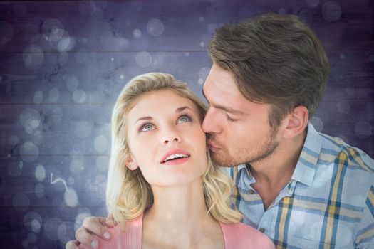 Handsome man kissing girlfriend on cheek against blue abstract light spot design