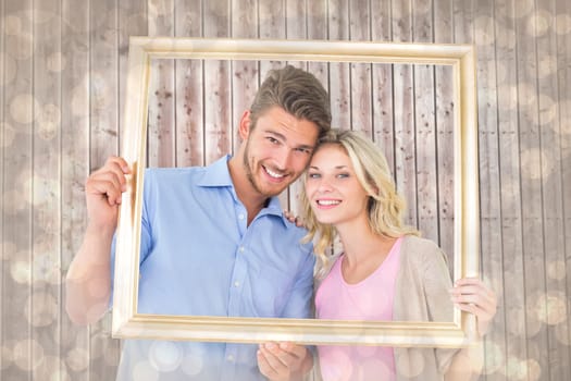 Attractive young couple holding picture frame against light glowing dots design pattern