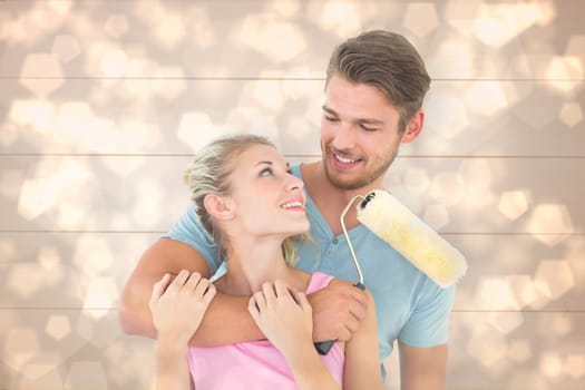 Young couple hugging and holding paint roller against light glowing dots design pattern