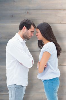 Angry couple facing off after argument against pale grey wooden planks