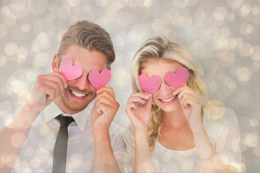 Attractive young couple holding pink hearts over eyes against light glowing dots design pattern