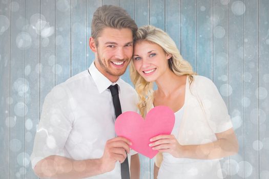 Attractive young couple holding pink heart against grey abstract light spot design