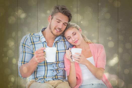 Attractive young couple sitting holding mugs against black abstract light spot design