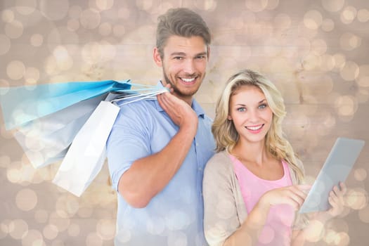 Attractive young couple holding shopping bags using tablet pc against light glowing dots design pattern