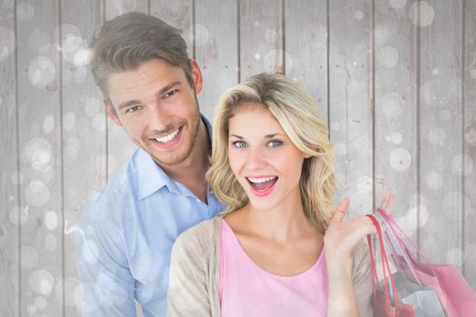 Attractive young couple holding shopping bags against grey abstract light spot design