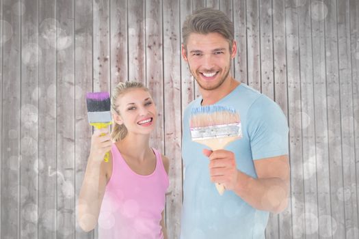 Young couple smiling and holding paintbrushes  against grey abstract light spot design