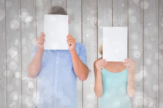 Young couple holding pages over their faces against grey abstract light spot design