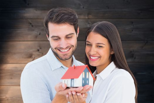 Attractive young couple holding a model house against wooden planks background