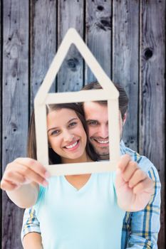 Happy young couple with house shape against grey wooden planks