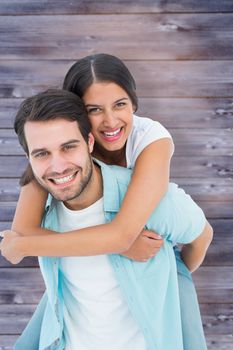 Happy casual man giving pretty girlfriend piggy back against faded grey wooden planks