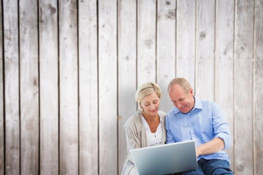 Happy mature couple using laptop against wooden planks