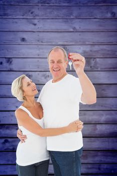 Mature couple smiling at camera with new house key against wooden planks background