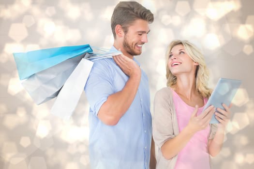 Attractive young couple holding shopping bags looking at tablet pc against light glowing dots design pattern