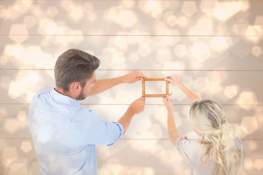 Attractive young couple hanging a frame against light glowing dots design pattern