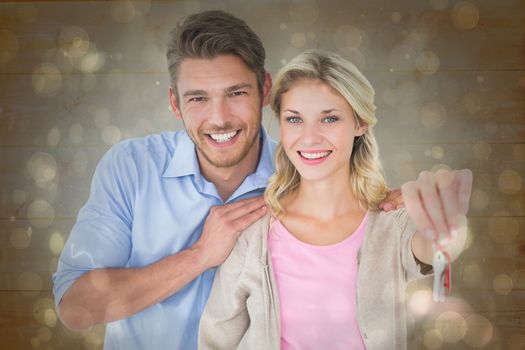 Attractive young couple showing new house key against black abstract light spot design