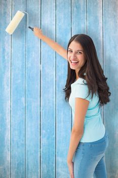 Happy young brunette painting with roller against wooden planks