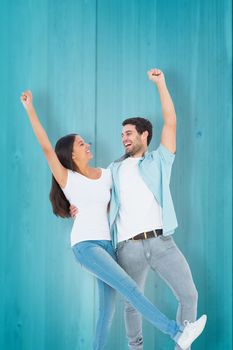 Happy casual couple cheering together against wooden planks background