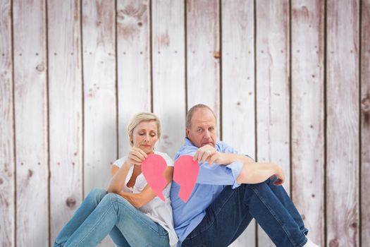 Sad mature couple holding a broken heart against wooden planks