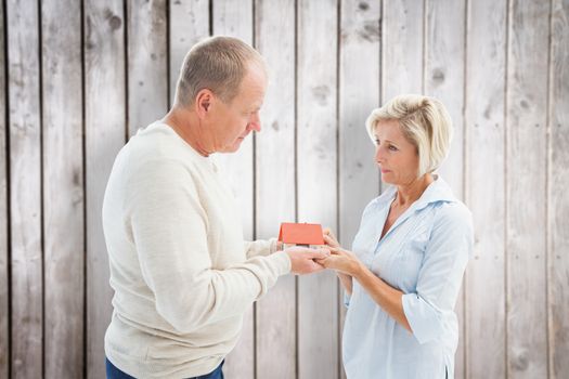 Serious mature couple with model house against wooden planks