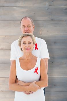 Mature couple supporting aids awareness together against pale grey wooden planks
