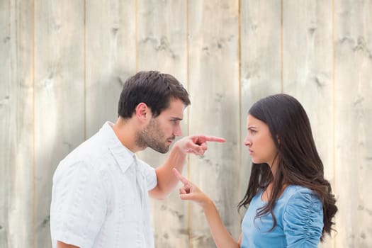 Angry couple pointing at each other against pale wooden planks