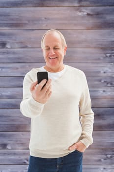 Happy mature man sending a text against faded grey wooden planks