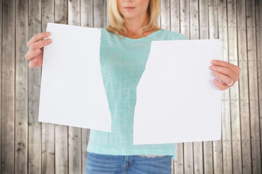 Serious woman holding torn sheet of paper against wooden planks background