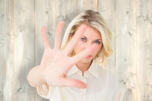 Pretty blonde holding hand up to camera against pale wooden planks