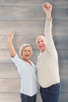 Happy mature couple cheering at camera against pale grey wooden planks